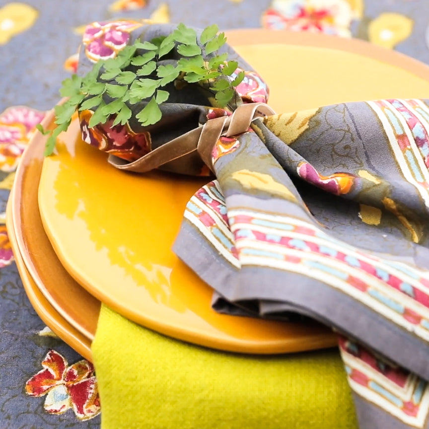 Close-up of Pansy Napkins Red & Grey, Set of 6 showcasing floral and striped patterns with yellow plates and greenery