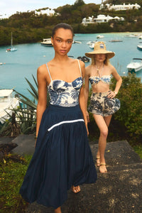 The Allegra Skirt in Navy paired with Nevis One Piece in Bermuda Toile in front of ocean. 