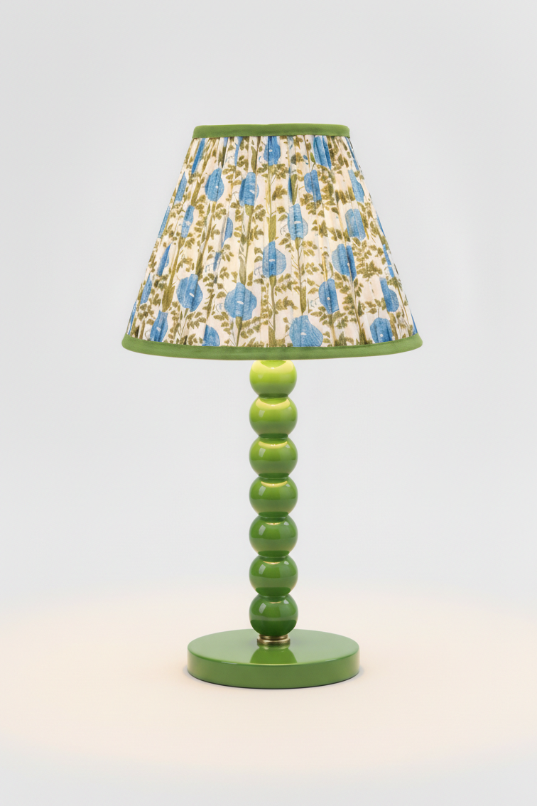 10-inch pleated blockprint empire lampshade in Araminta Blue on a green ceramic lamp base, illuminated to highlight the blue floral and green leaf design.