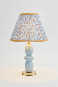 10-inch pleated blockprint empire lampshade with sky blue daisy pattern, mounted on light blue ceramic table lamp with golden base, illuminated with warm light