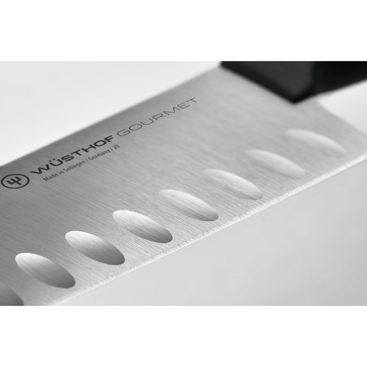 Close-up of 7-inch Wüsthof Gourmet santoku blade showing granton (hollow) scallops and branded logo on brushed stainless steel