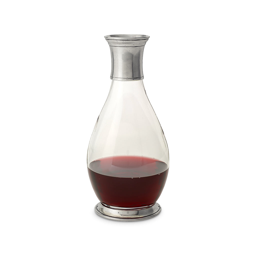 Front view of tall carafe with pewter collar and tiered top, clear glass body half-filled with red liquid on white background