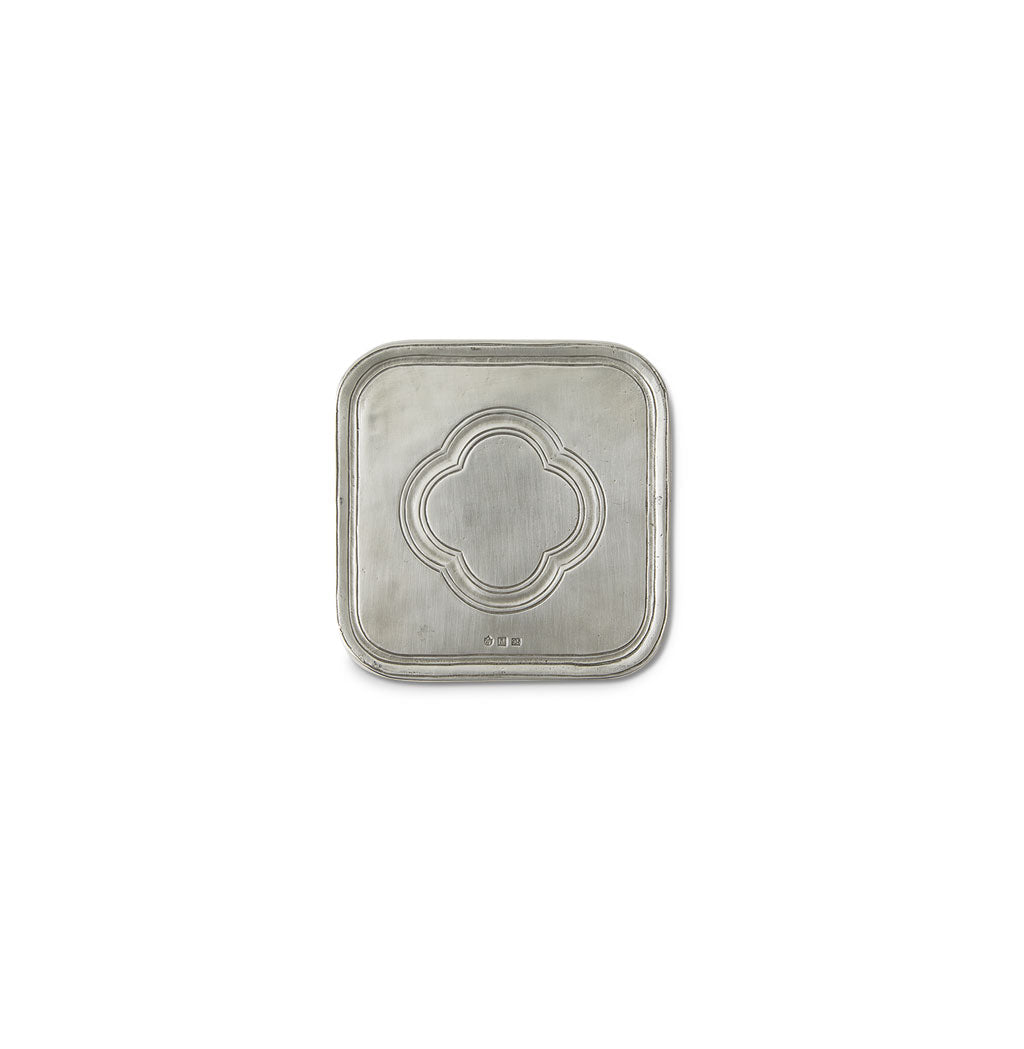 Top view of pewter square coaster showcasing embossed quatrefoil motif on white background
