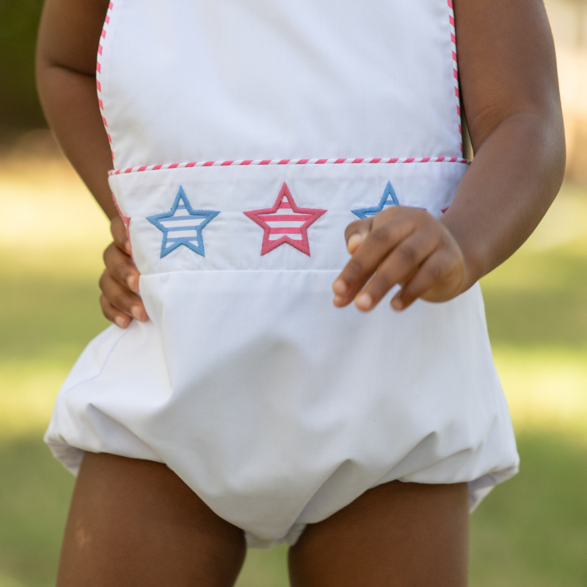Henry Duvall unisex baby sunsuit in white with red and blue star appliqué and criss cross straps, classic patriotic outfit for Memorial Day, 4th of July, and summer occasions