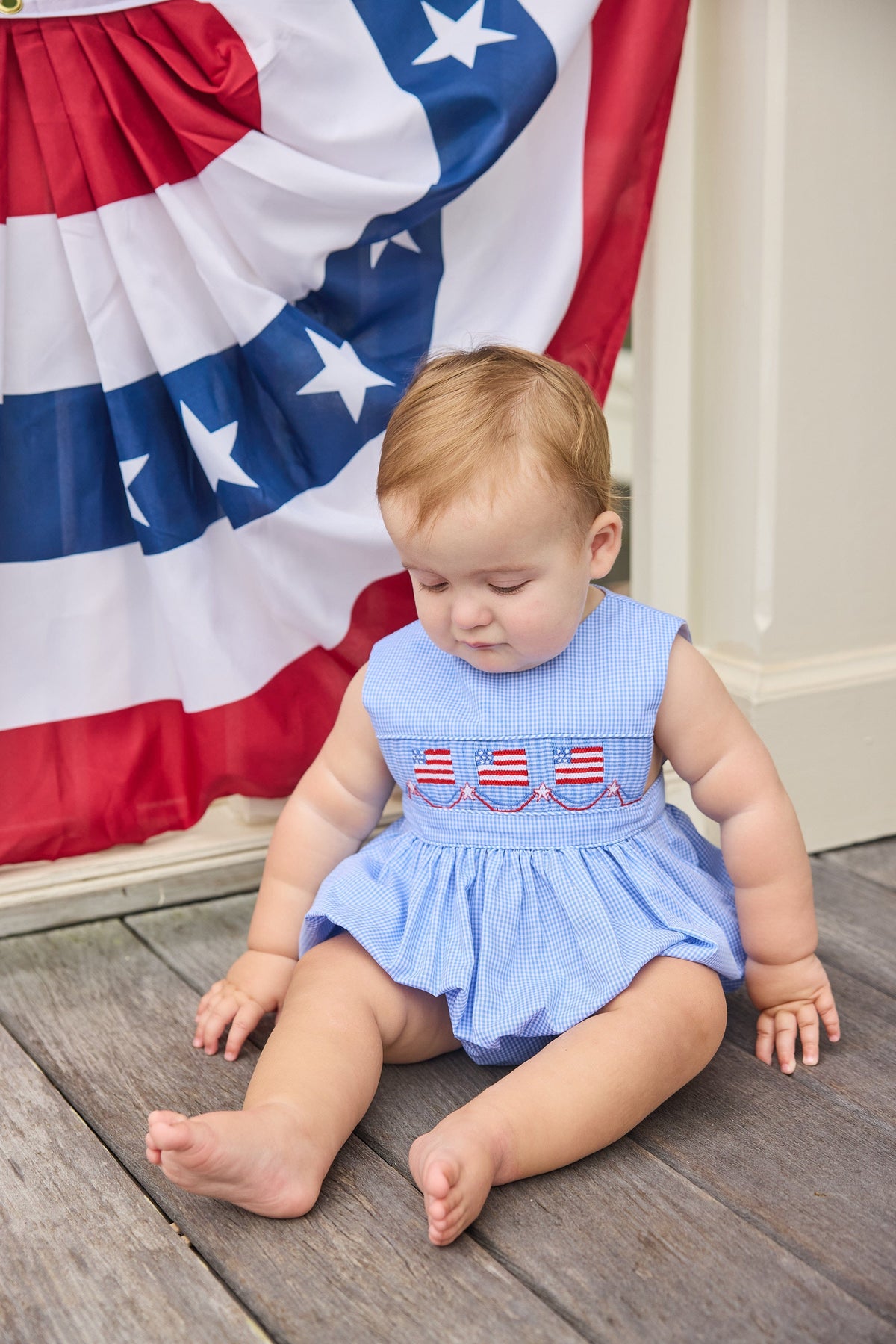 Little English traditional children's clothing.  Sleeveless bubble in royal blue mini check fabric and smocking at the chest with American flag bunting for baby boys