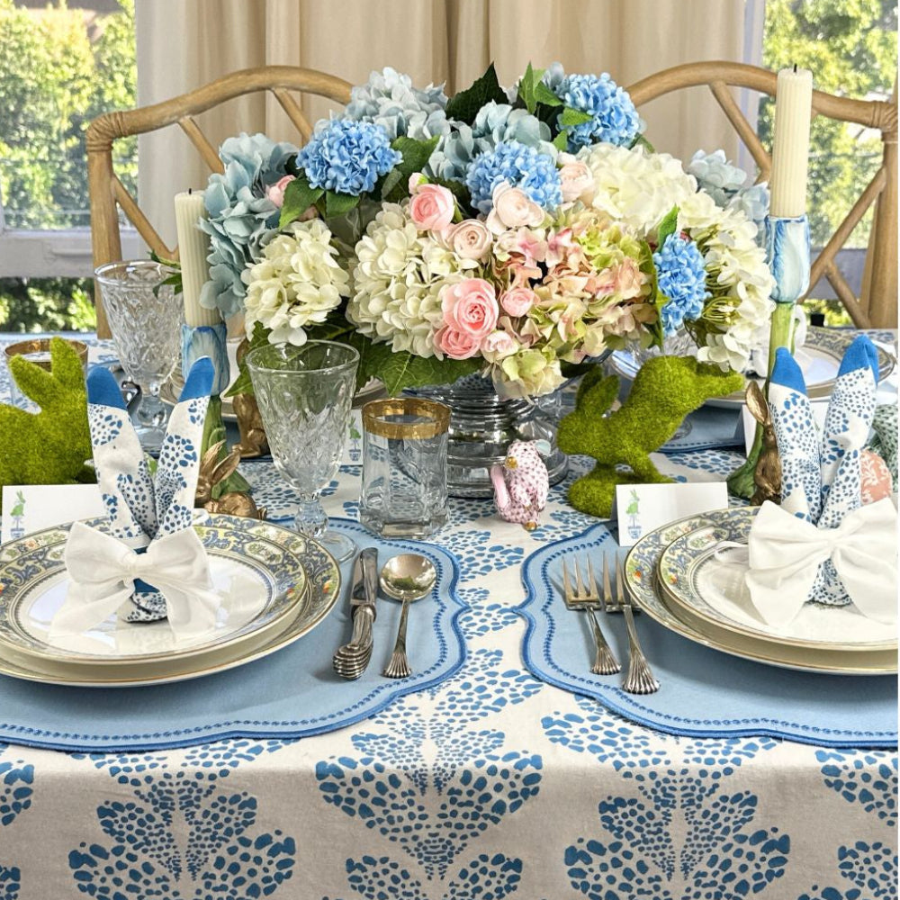 Elegant Easter table setting with floral centerpiece, blue and white tablecloth, and silverware.