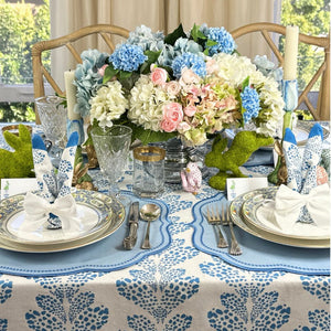 Elegant Easter table setting with floral centerpiece, blue and white tablecloth, and silverware.