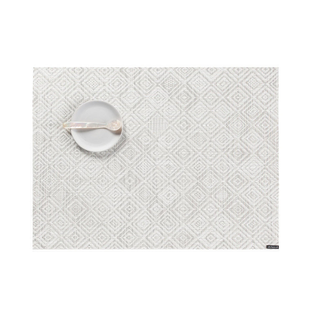 Top-down view of Mosaic Placemat showing light gray and white diamond mosaic weave with a small white dish and spoon