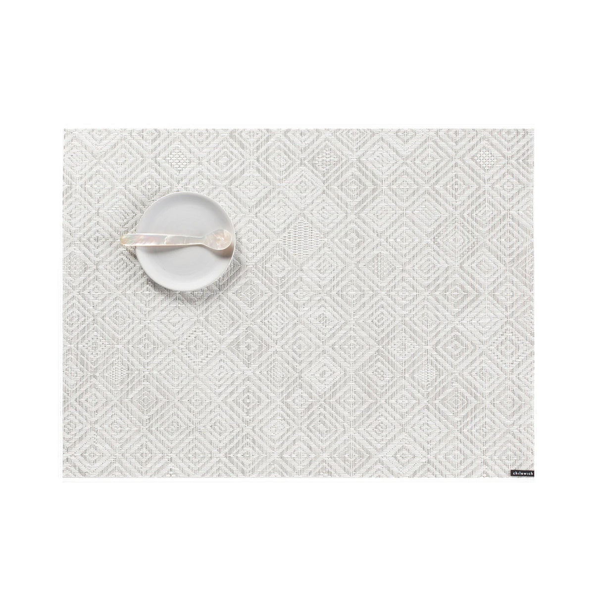 Top-down view of Mosaic Placemat showing light gray and white diamond mosaic weave with a small white dish and spoon