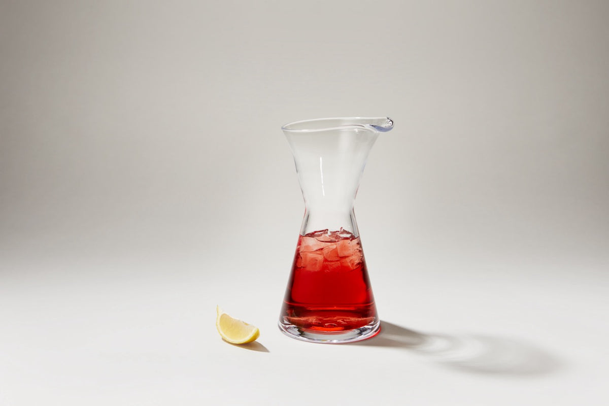 Front view of Westport Quartino carafe showcasing tapered double-cone silhouette with red beverage and ice on white background