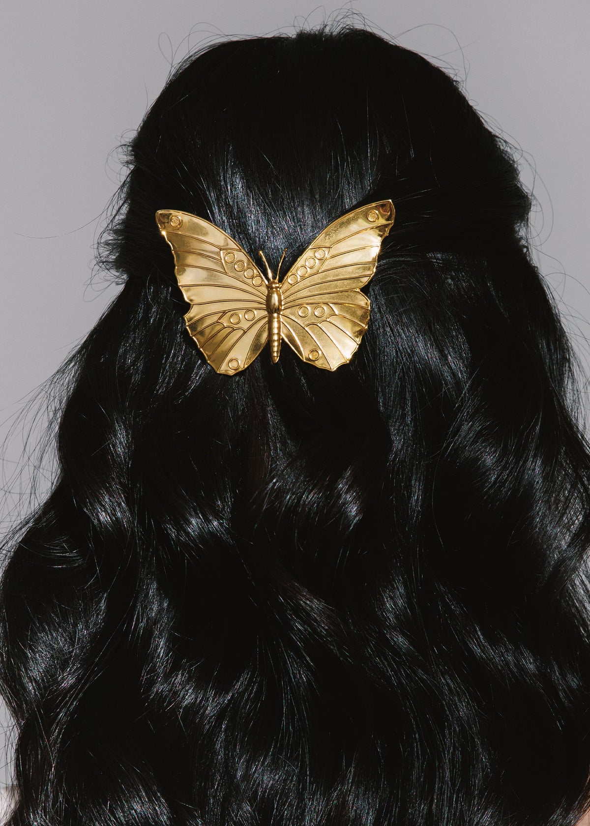 Front view of Caria Barrette in Gold showcasing its embossed butterfly design on black hair