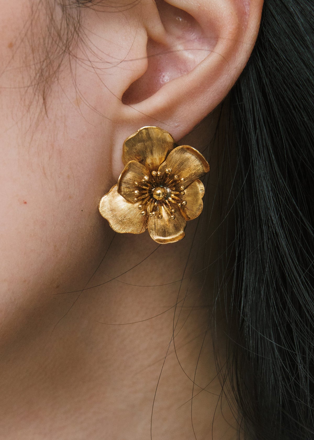 Close-up view of Kenna Earrings in Gold showcasing a sculpted flower earring with textured petals and stamen details on an ear