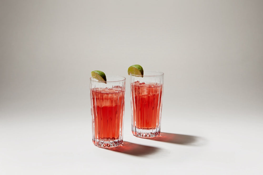 Front view of Montpelier Highball set of 2 showing vertical fluted ribbing, filled with red cocktails and lime wedges on a neutral background