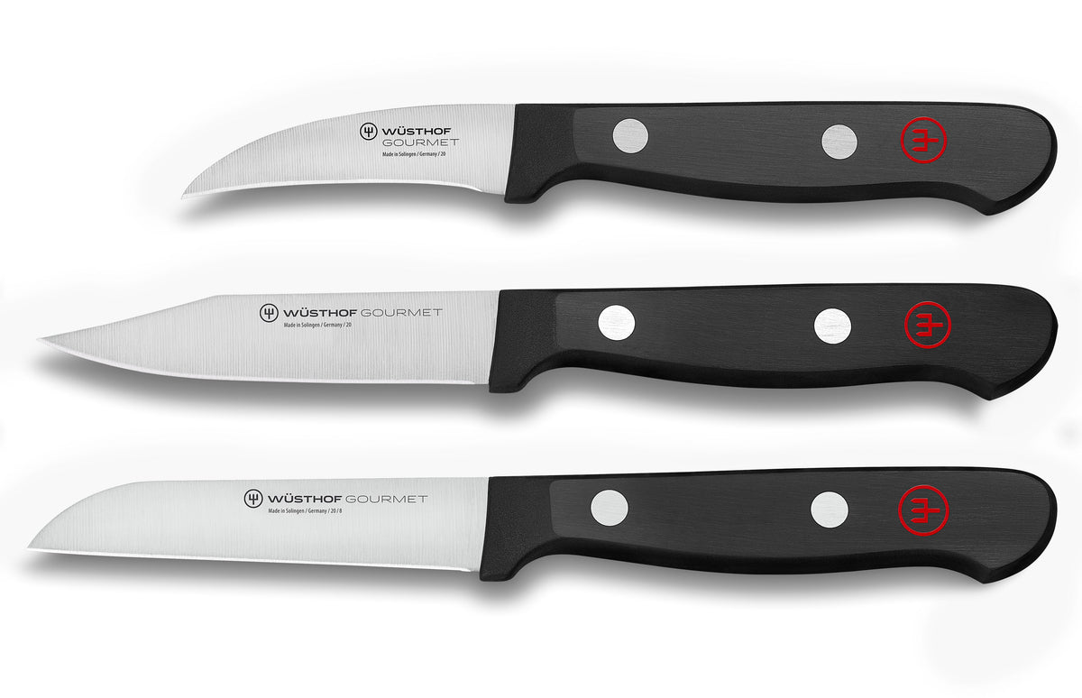 Flat lay of three Wusthof Gourmet paring knives with stainless steel blades and black riveted handles on white background