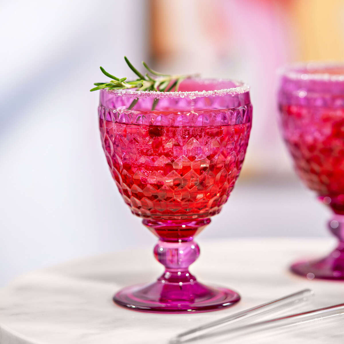 Close-up of Boston Berry red wine glass showing faceted berry-pink glass with sugared rim and rosemary garnish on a white tabletop