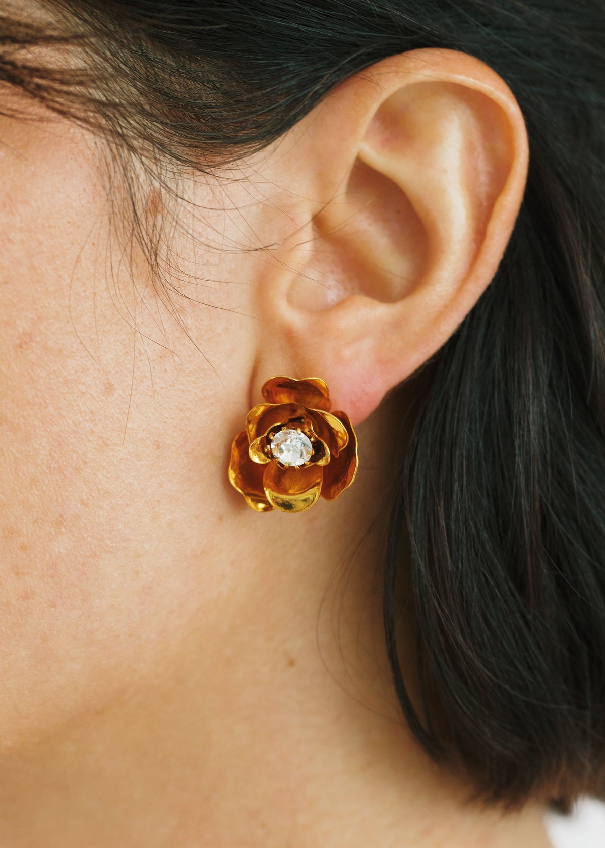 Close-up view of Lil Earrings in Crystal Antique Gold showcasing a blossom stud with center crystal on an ear