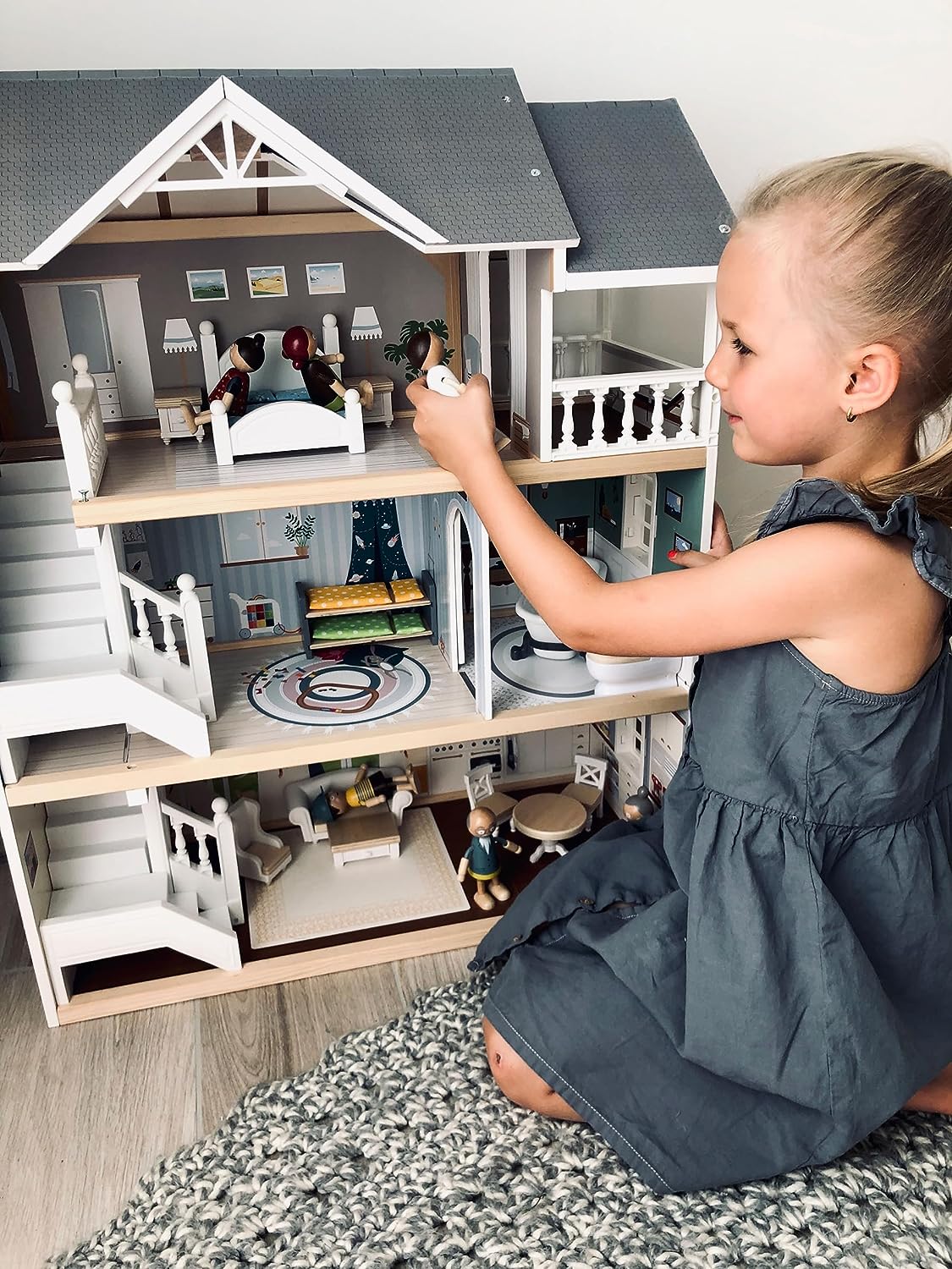Girl playing with a three-story wooden dollhouse, arranging furniture on the middle floor