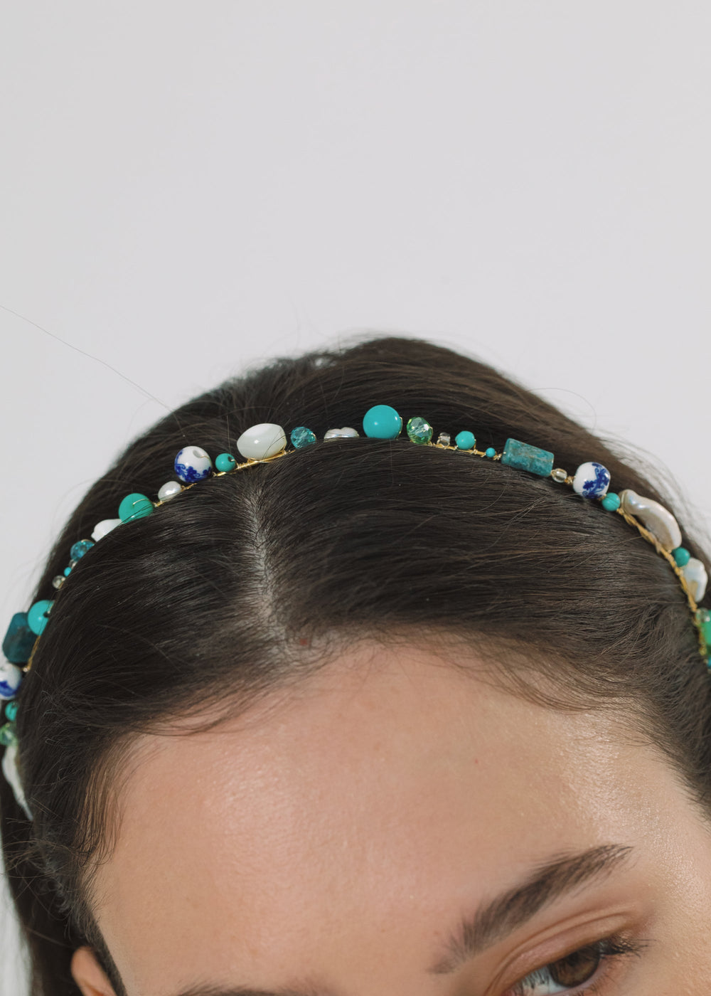 Close-up of Marietta headband worn by a model showing turquoise and white beads, pearls, and gold wire on a light background