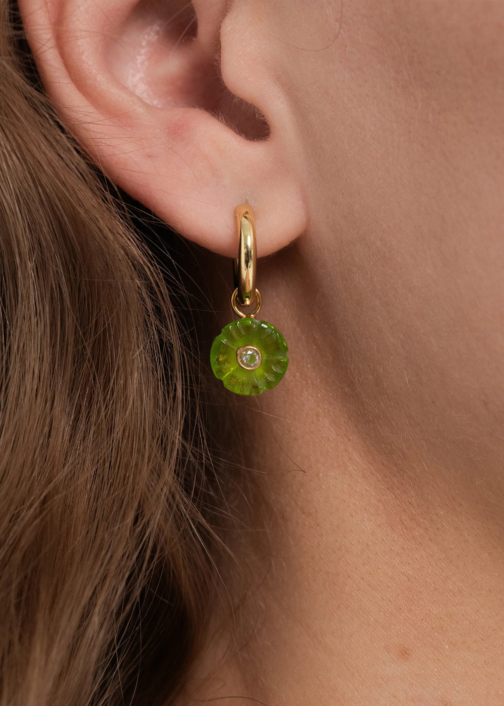 Close-up side view of Lillian huggie earring in peridot with hand-carved floral charm and central crystal on model’s ear