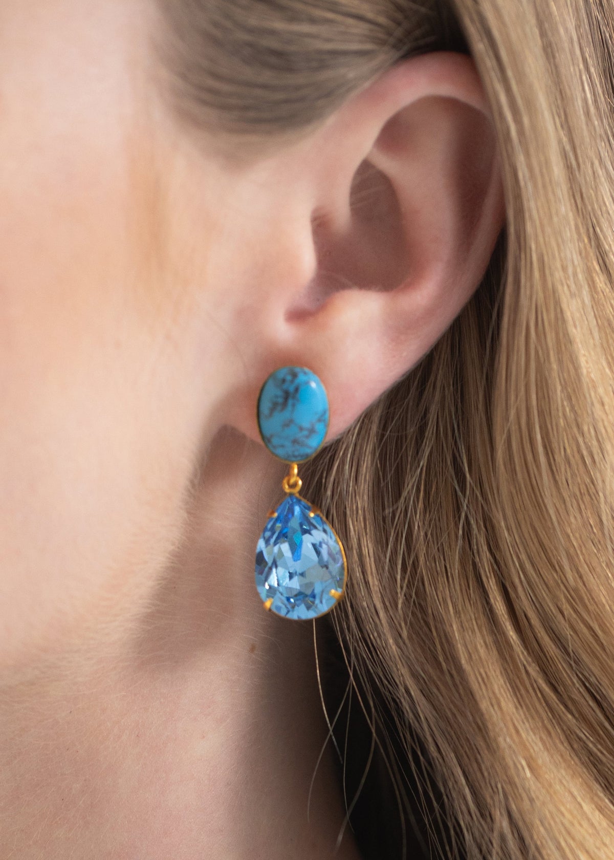 Close-up of Linette Earrings in Turquoise showcasing genuine turquoise and pear-shaped crystal drop on a model’s ear