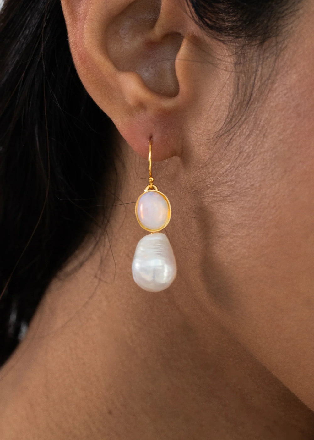 Close up of Tatum Earrings in Opal on a model showing an oval opal cabochon above a baroque freshwater pearl on a gold-filled ear wire