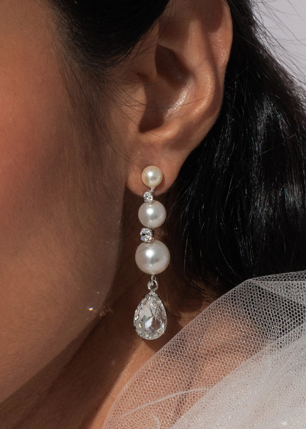 Close-up of Corisande earrings in silver showing graduated pearls and pear-cut crystal teardrop on ear