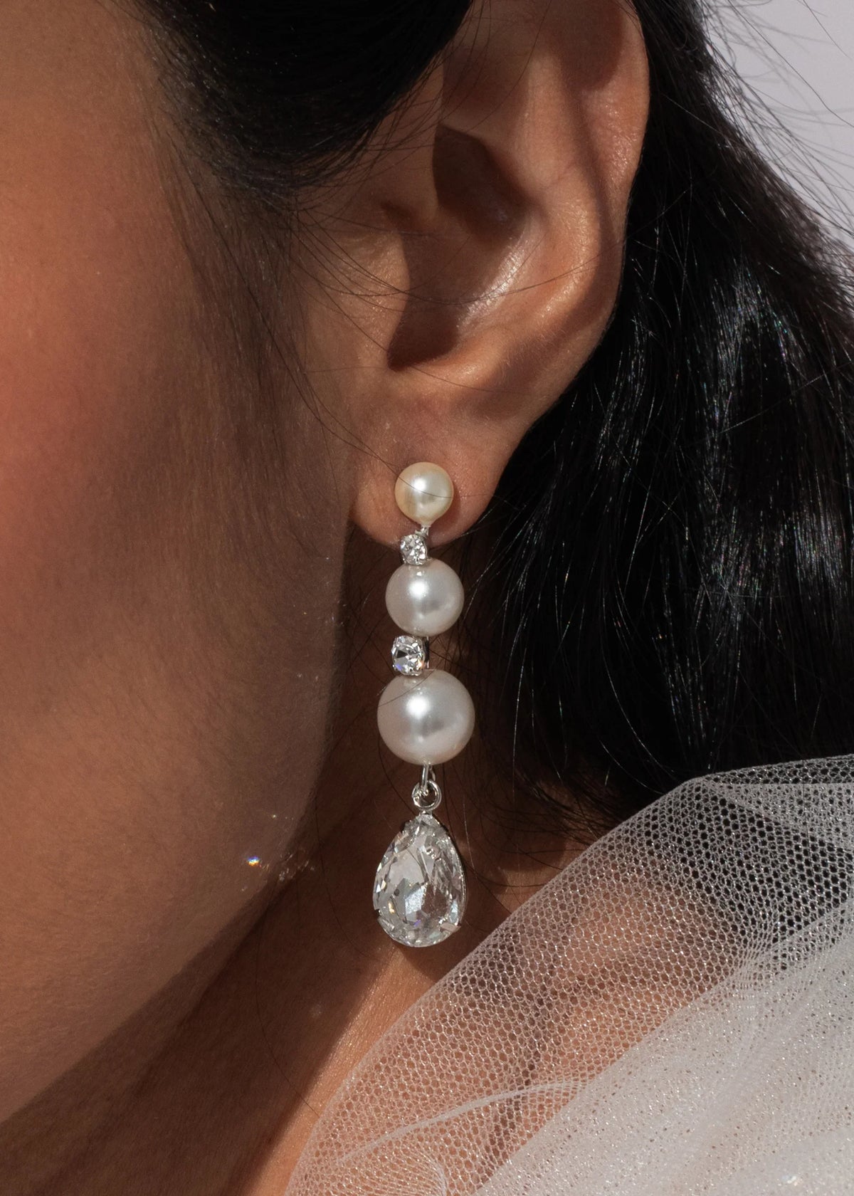 Close-up of Corisande earrings in silver showing graduated pearls and pear-cut crystal teardrop on ear