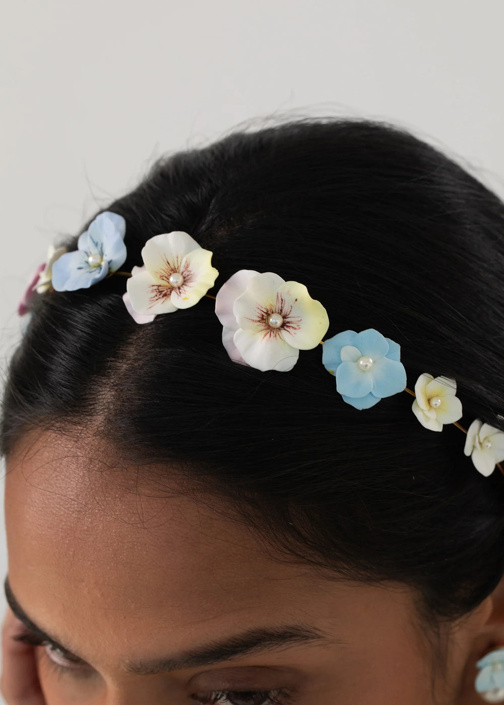 Close-up of model wearing Anarosa Headband in Garden Multi showing clay flower appliques with pearl centers on a light background