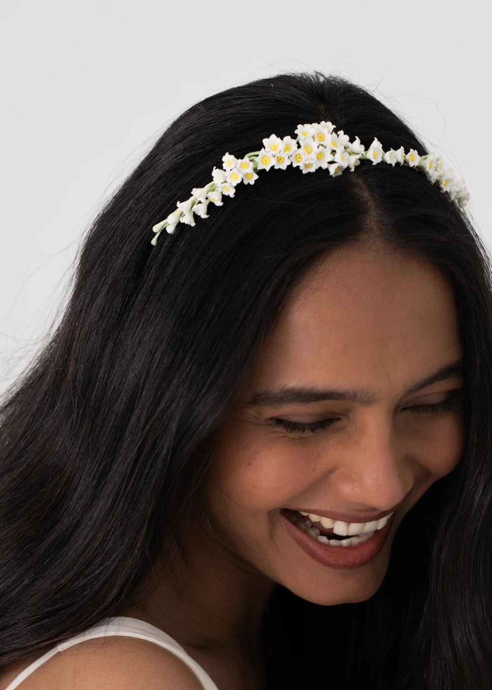 Angled close up of Victoria Headband in Lily showing white clay lily of the valley flowers on a thin band worn on a model