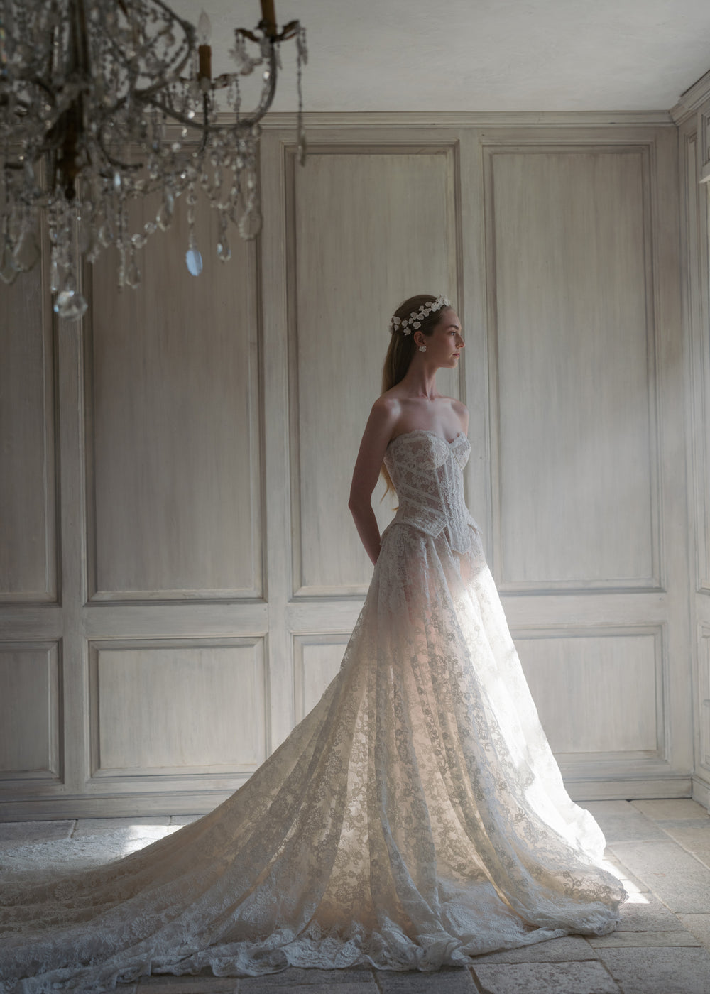 Model wearing Karissa earrings in cream, standing in profile in a sunlit paneled room while wearing a lace bridal gown