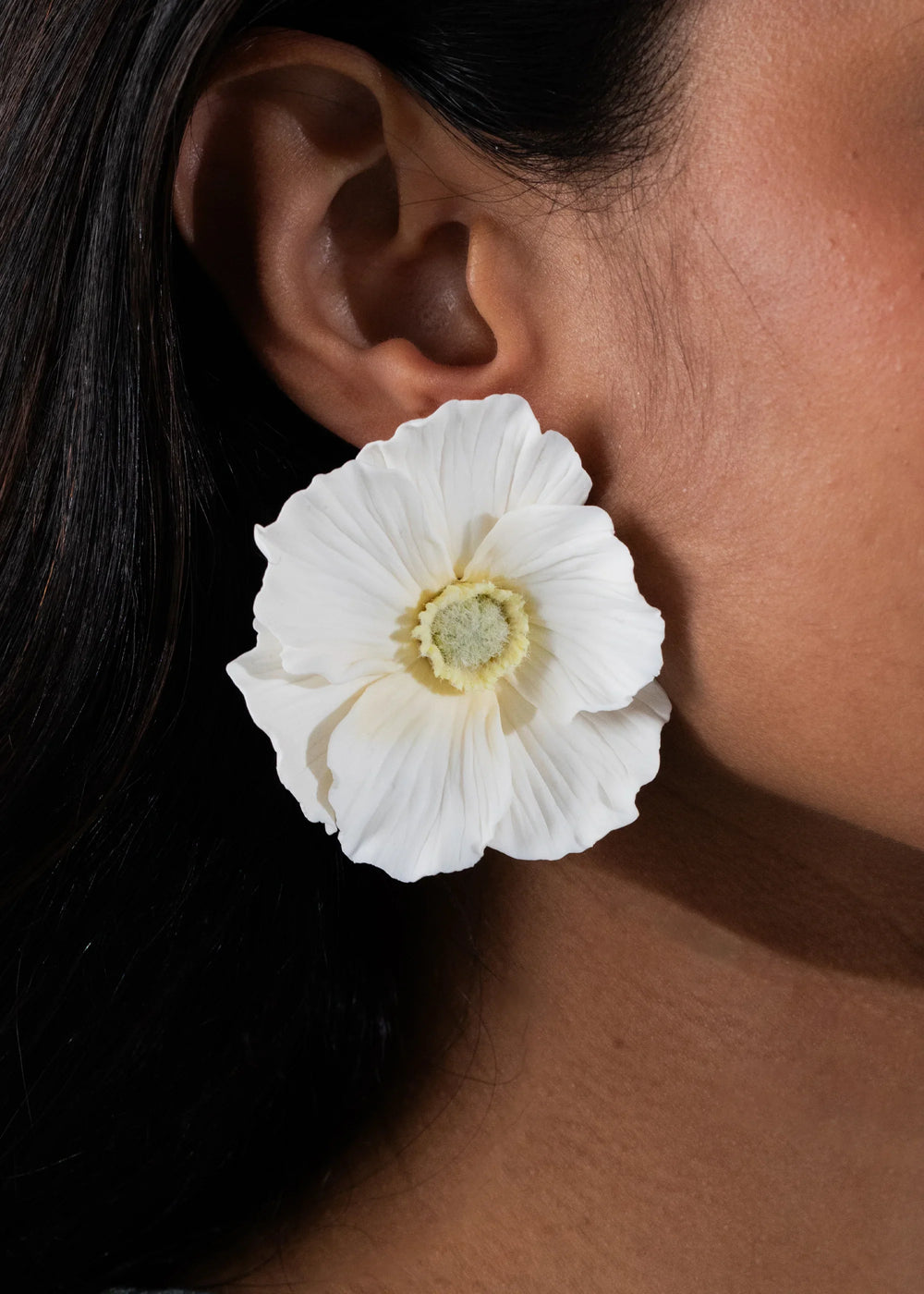 Close-up side view of Demetria earrings in cream showing a large hand-formed white poppy clay flower on the ear against dark hair