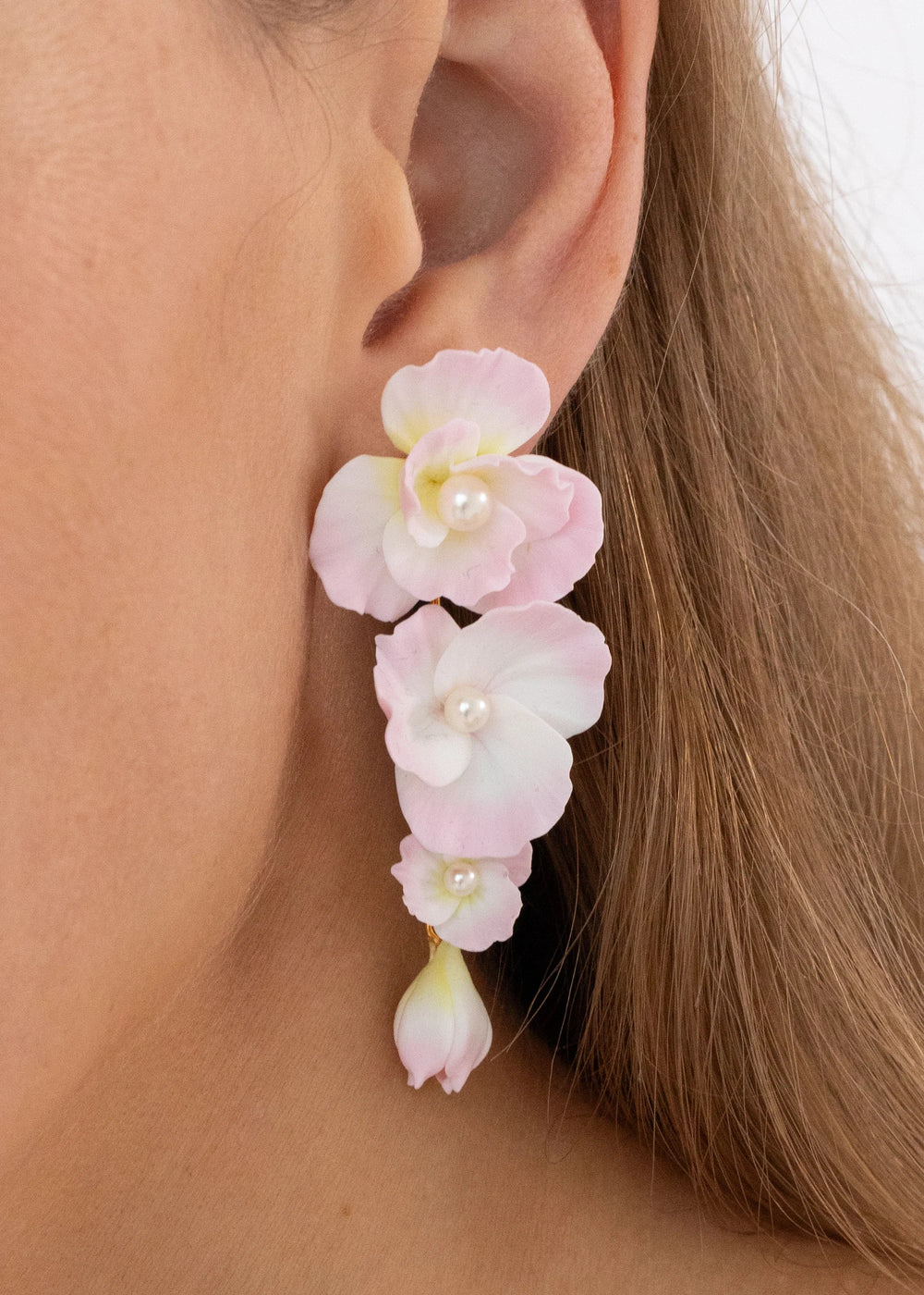 Close-up of Mariam earrings in Peony showcasing cascading pale-pink hand-pressed clay flowers with pearl centers on a model’s ear