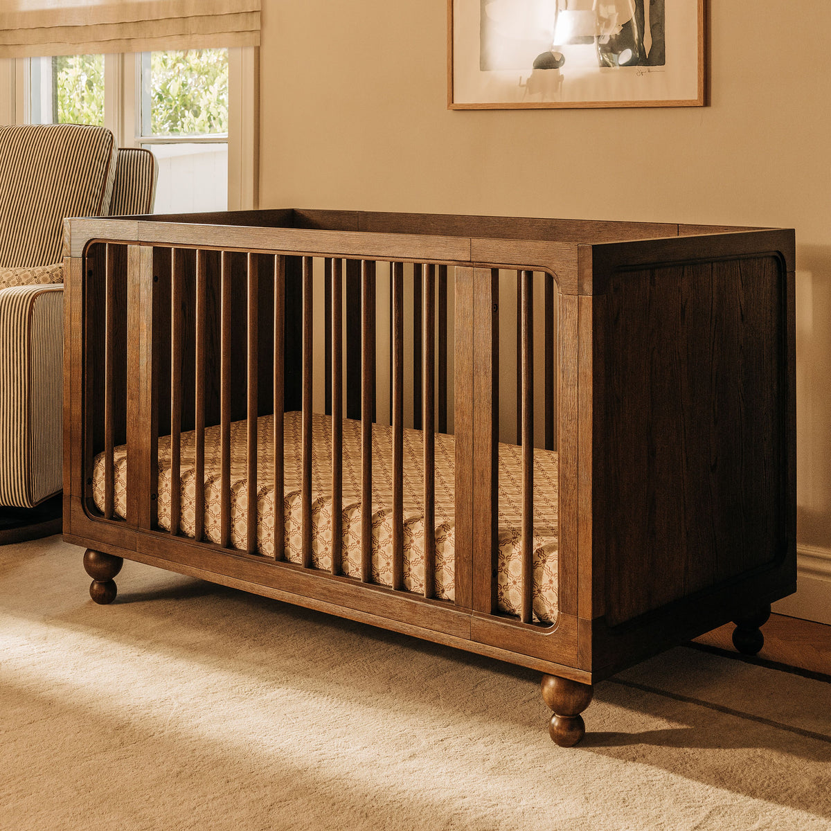 Front angled view of the Toffee Astre All Stages 8 in 1 crib showcasing vertical slats and caster wheels in a warm nursery