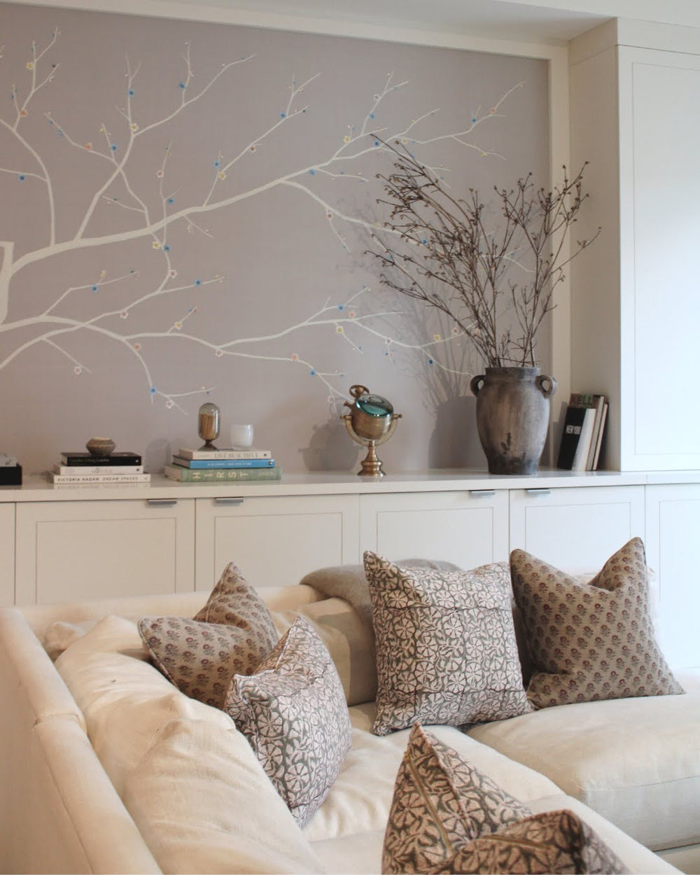 Front view of Shoreditch pillows showcasing beige floral linen pattern on a cream sofa with painted branch mural and white cabinets backdrop