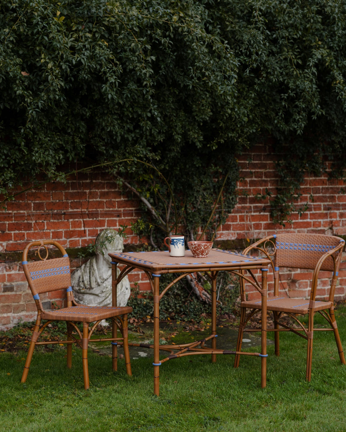 Three-quarter view of Juliette dining table with woven rattan top and hickory brown frame and matching chairs in a garden