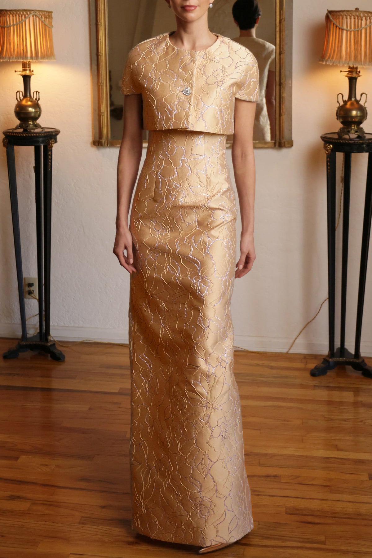 Front view of silk capelette with short sleeves and single diamanté button over matching floral jacquard gown in room