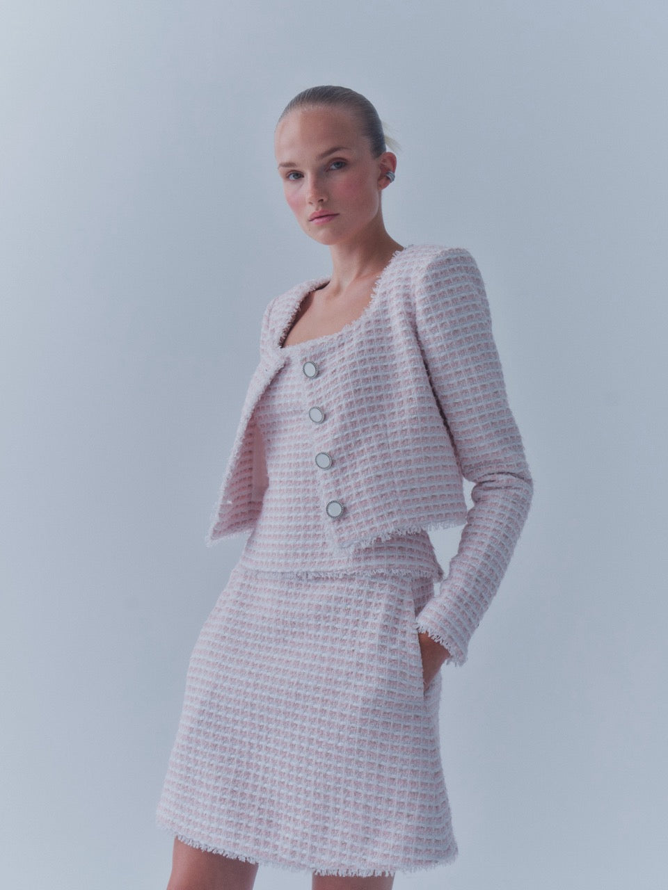 Three-quarter view of The Winifred Jacket in pink and white tissage, cropped silhouette with silver enamel buttons and frayed edges on a pale background