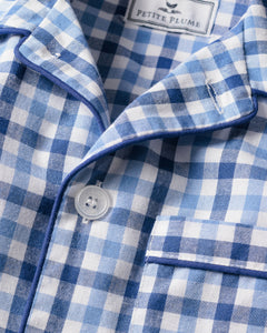 A close-up of the Kids Twill Pajama Set in Royal Blue Gingham by Petite Plume reveals a gingham print with a button, pocket, and neck label. Blue piping outlines the classic pajama set.
