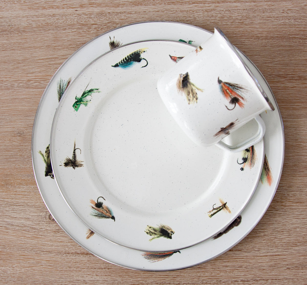 Overhead view of Dinner Plates in Flying Fish, Set of 4 showcasing illustrated fishing flies and stainless steel trim on a wood background