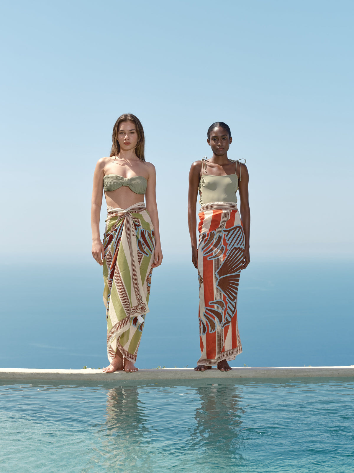 Front view of De La Falaise cotton silk sarong showcasing orange ornament stripes on a model beside the ocean