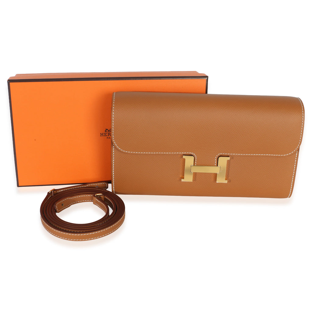 Front view of Hermès Gold Epsom Constance Long Wallet To Go showcasing H clasp and strap with orange box on white background
