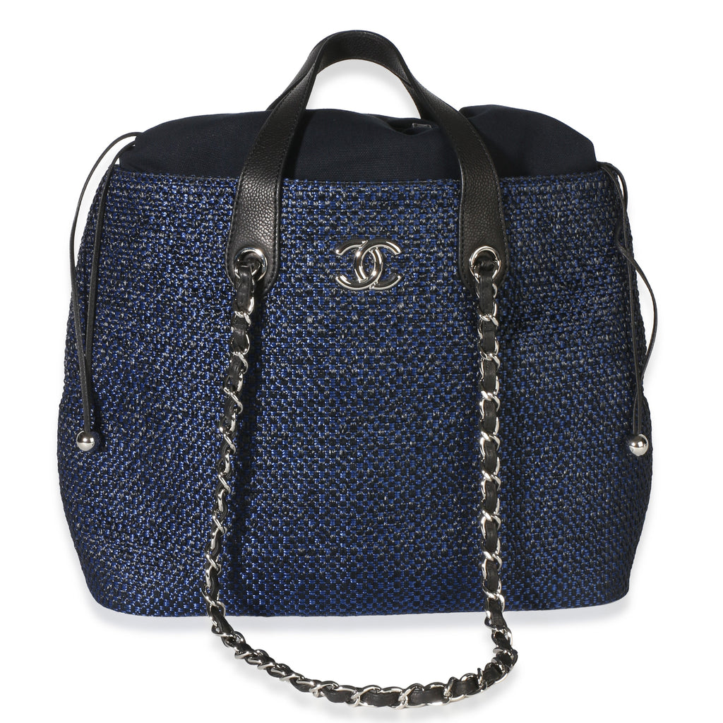 Front view of Chanel navy blue raffia CC expandable tote with silver tone logo and drawstring closure on white background