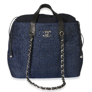Front view of Chanel navy blue raffia CC expandable tote with silver tone logo and drawstring closure on white background