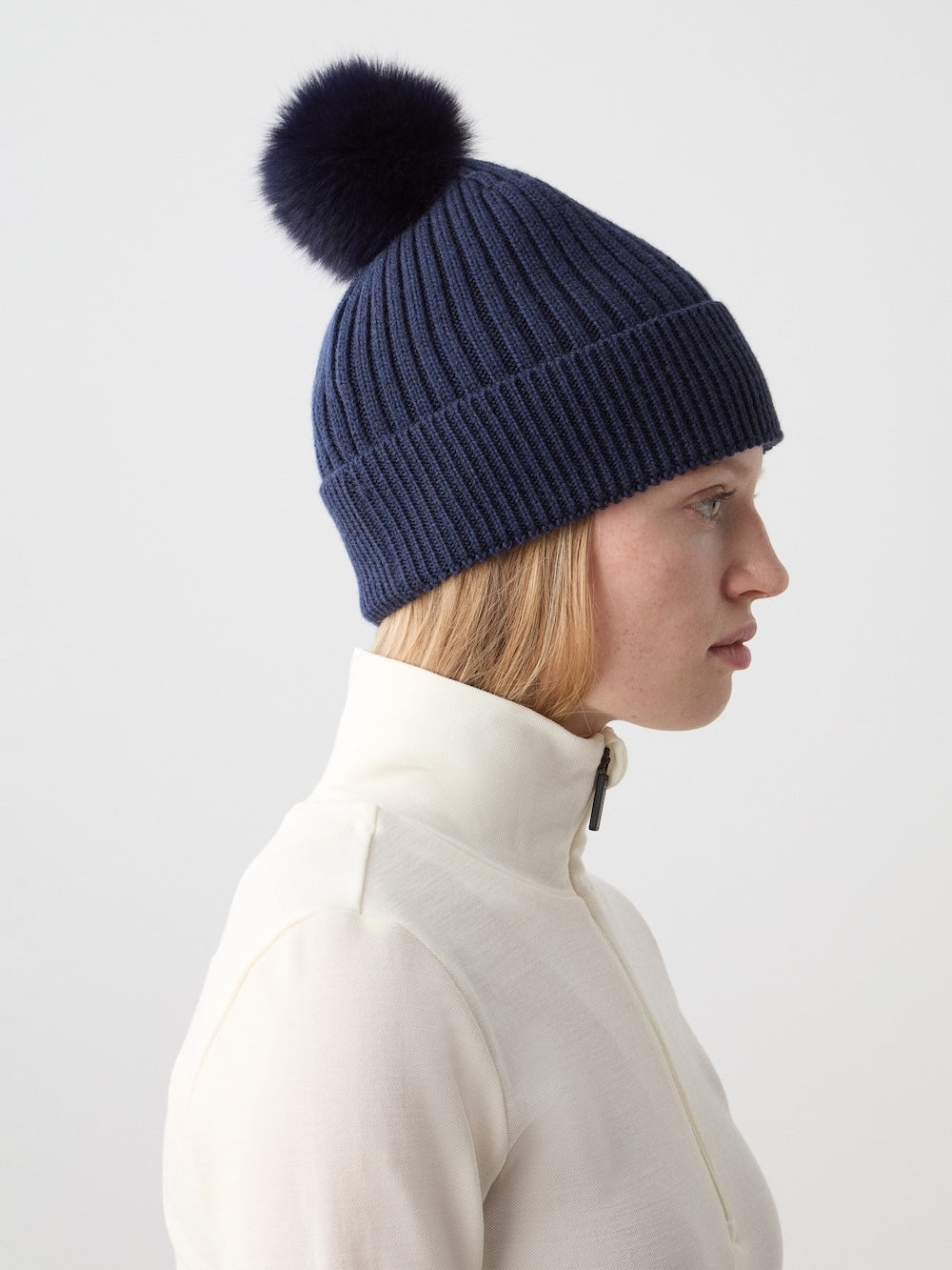 Side view of Hemsedal Hat on model showcasing navy ribbed merino wool and dark fur pom pom on light background