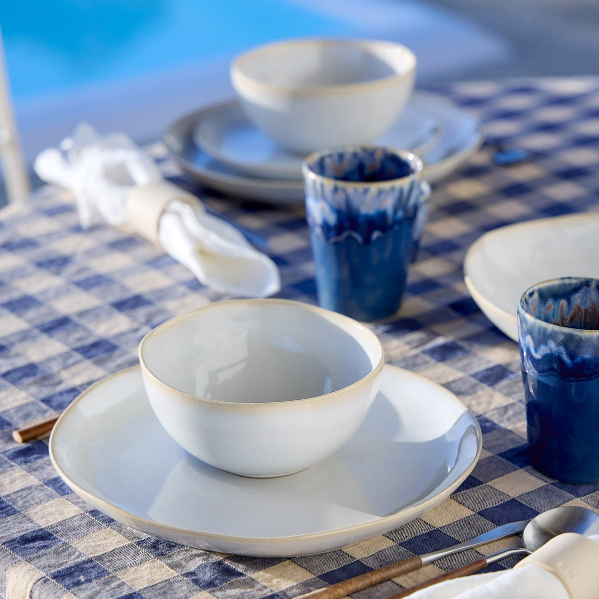 Close-up of Brisa Collection salad plate and bowl in Branca showing soft white glaze with a subtle blue rim on a blue checkered tablecloth