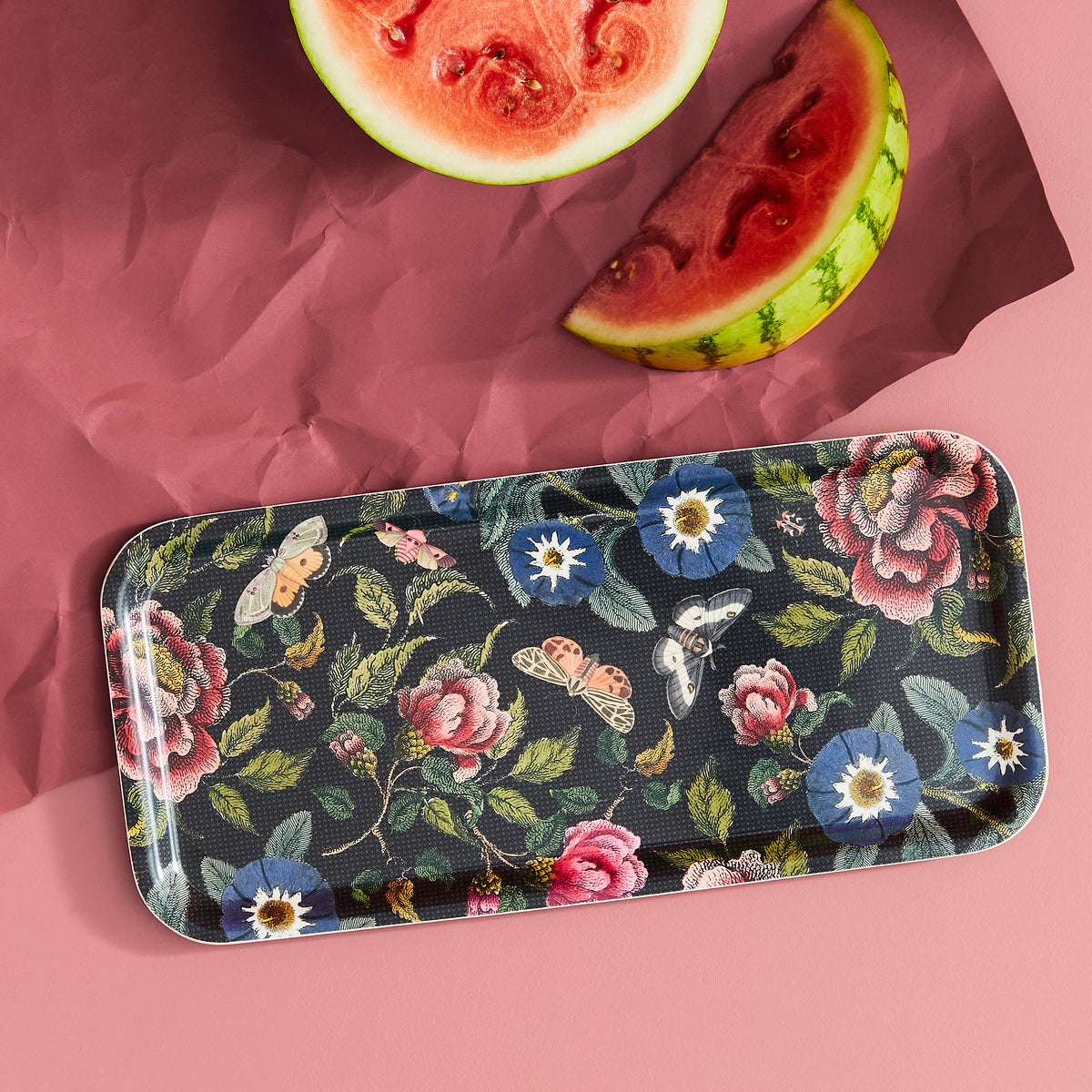 Close-up of Creatures of Curiosity Long Birch Tray showcasing dark floral pattern with watermelon on a pink background