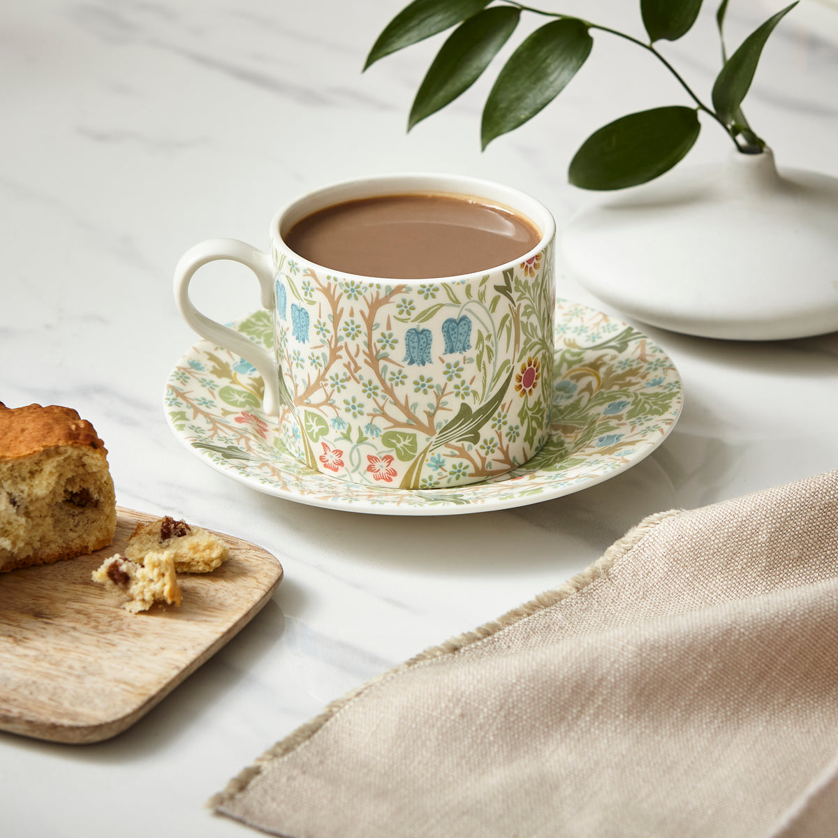 Front view of Morris & Co. Teacup & Saucer in Blackthorn showcasing vibrant flowers and dense greenery on a white tabletop