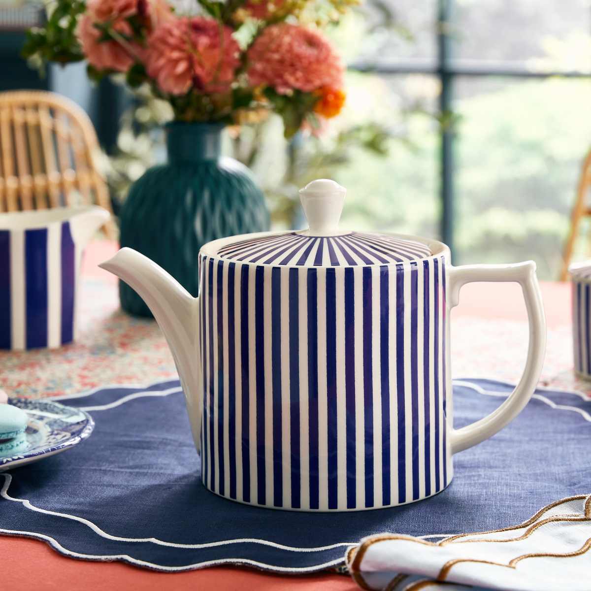 Front view of Steccato Teapot showcasing cobalt blue stripes on its body and lid with a floral dining table background
