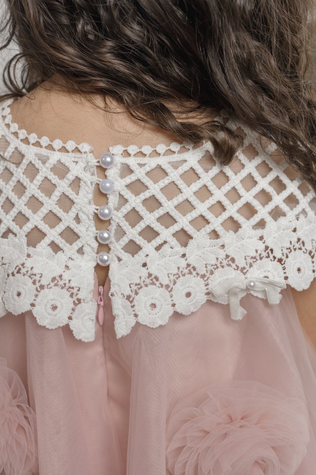 Close up details of lace and pearl details on girls pink tulle dress with flower details