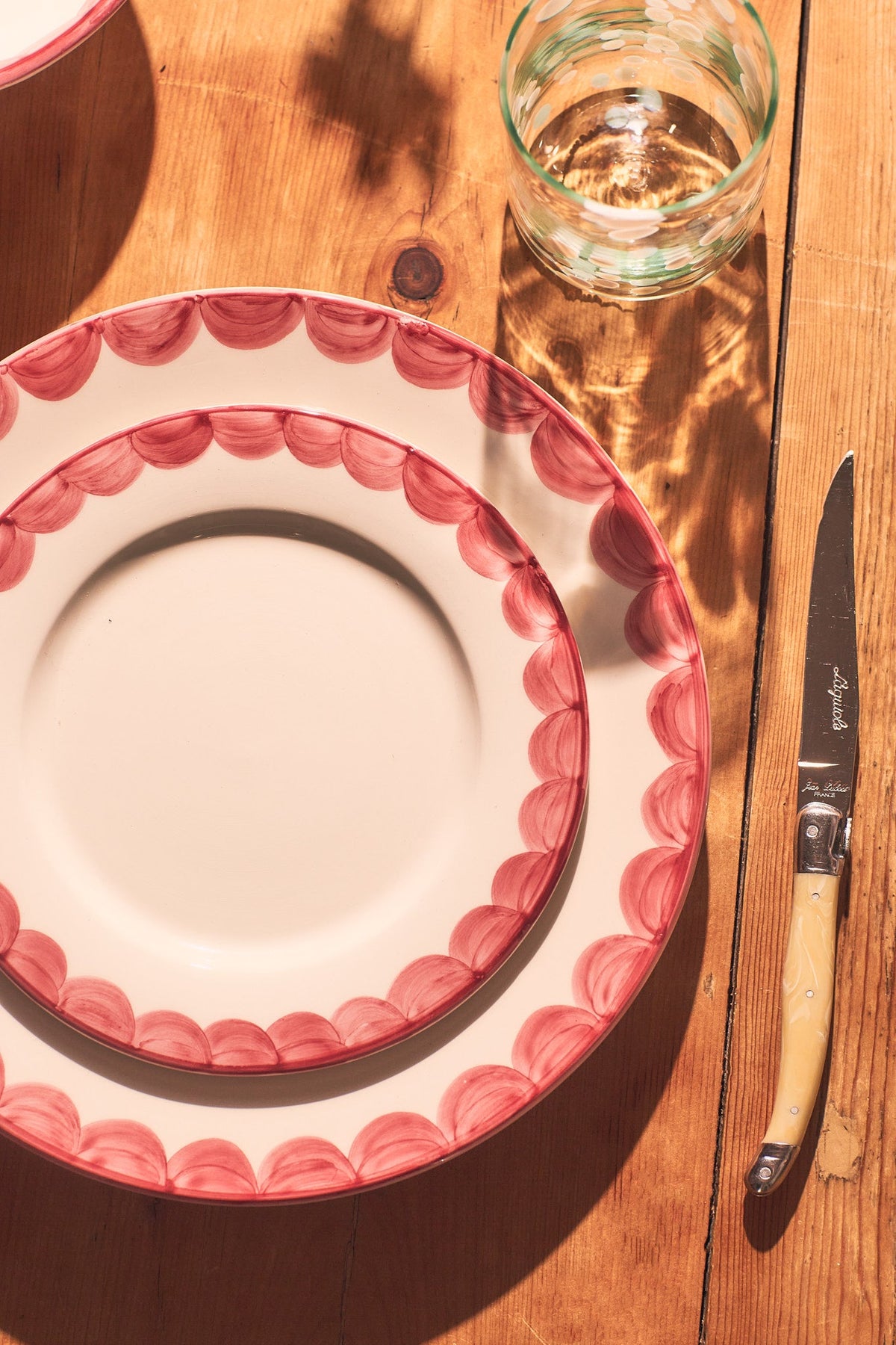 Top view of Pink Scallop Side Plate showcasing its scalloped pink rim on a wooden table with glass and utensils